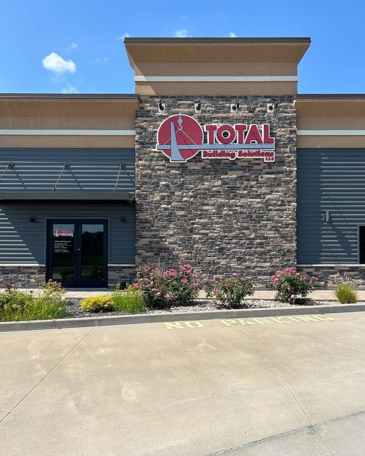 Front of the Total Building Solutions office with the logo sign on the stone tower and flowering shrubs