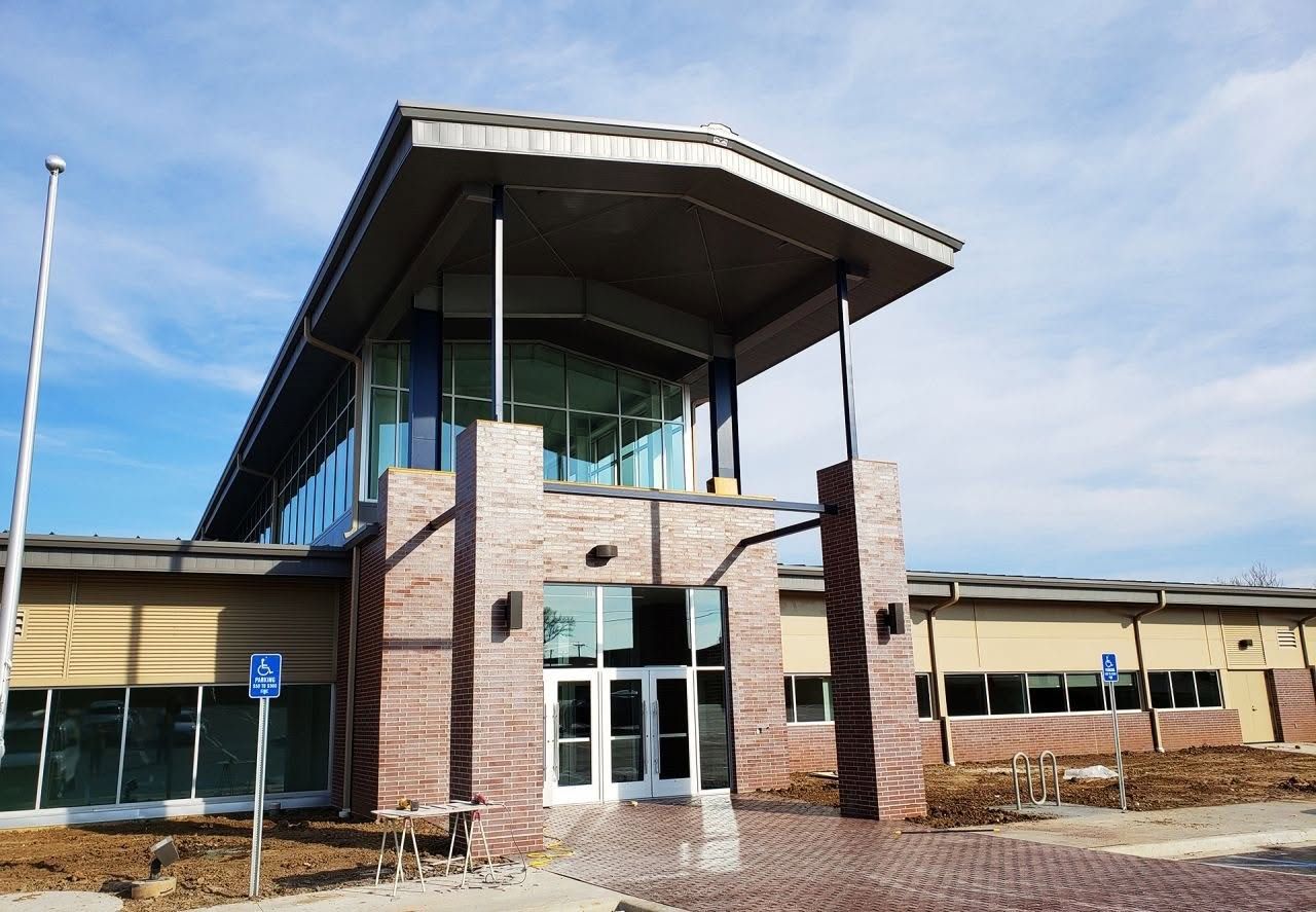 Finished building entrance with brick columns, a glass curtain wall and a wide overhanging canopy roof
