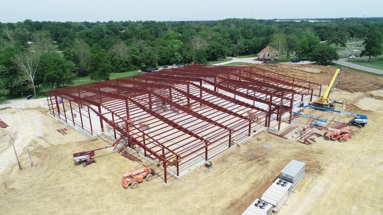 Aerial view of red-iron rigid steel frames erected on a concrete slab, with lifts and a crane on site